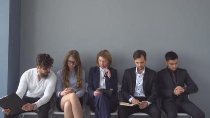 Unemployed expect interviews sitting on chairs in the hallway of an office building.