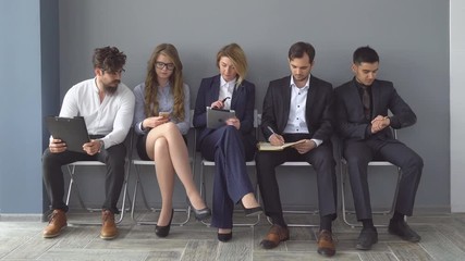 Unemployed expect interviews sitting on chairs in the hallway of an office building.