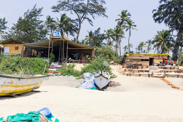 View of a tropical sandy beach with bungalows and boats on a background of palms.