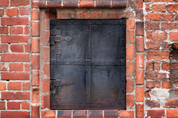 The red brick wall of old building with window shuttered partially by iron shutters with iron treillage. Moscow. Russia.