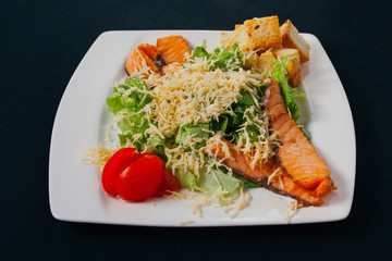 Grilled salmon with spinach and seasonal vegetables salad on white plate, black background