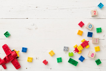 Top view on wooden cubes with numbers and colorful toy bricks and  plane on white wooden background. Toys in the table - obrazy, fototapety, plakaty