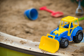 Closeup of bright blue and yellow tractor and children plastic shovel and pail in the sandbox. Baby's toys outdoor.