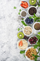 Healthy fitness food from fresh fruits, berries, greens, super food: kinoa, chia seeds, flax seed, strawberry, blueberry, kiwi, cherry, almonds, walnuts, mint, oatmeal natural flakes on a light marble