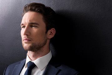 serious man with stubble is standing against dark background