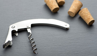 Close-up of corkscrew on blackboard next to several corks. Horizontal studio shot.