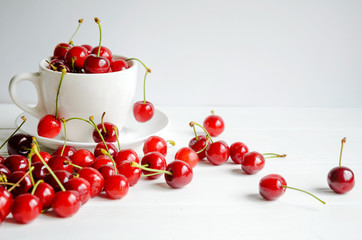 Obraz na płótnie Canvas Ripe sweet cherries in a white cup on white wooden background, tasty and healthy dessert