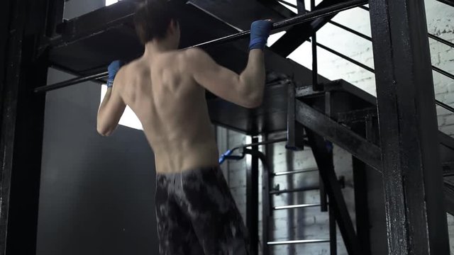 An athlete in training does pull-ups in a boxing gym. Tired and sweaty athlete.