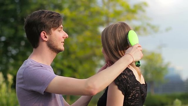 A young guy combing his girlfriend's hair