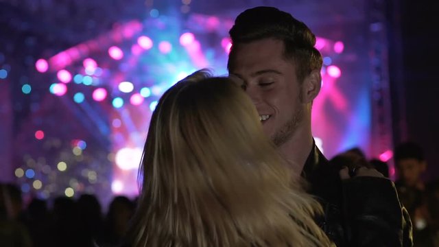 Attractive man and woman dancing and kissing at music festival, happiness