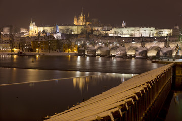 Fototapeta na wymiar Night romantic snowy Prague gothic Castle and St. Nicholas' Cathedral with Charles Bridge, Czech republic
