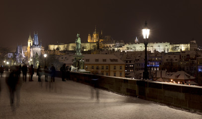 Obraz premium Night snowy Prague Lesser Town with gothic Castle, Bridge Tower and St. Nicholas' Cathedral from Charles Bridge with its baroque Statues, Czech republic