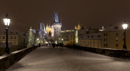 Fototapeta na wymiar Night snowy Prague Lesser Town with gothic Castle, Bridge Tower and St. Nicholas' Cathedral from Charles Bridge with its baroque Statues, Czech republic