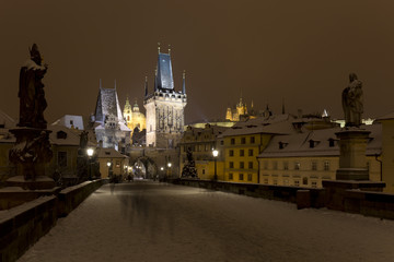 Obraz premium Night snowy Prague Lesser Town with gothic Castle, Bridge Tower and St. Nicholas' Cathedral from Charles Bridge with its baroque Statues, Czech republic