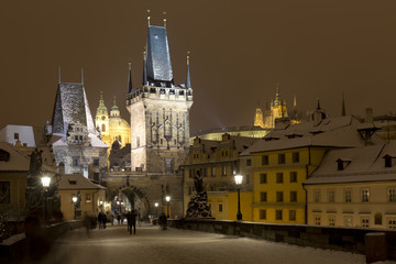 Obraz premium Night snowy Prague Lesser Town with gothic Castle, Bridge Tower and St. Nicholas' Cathedral from Charles Bridge with its baroque Statues, Czech republic