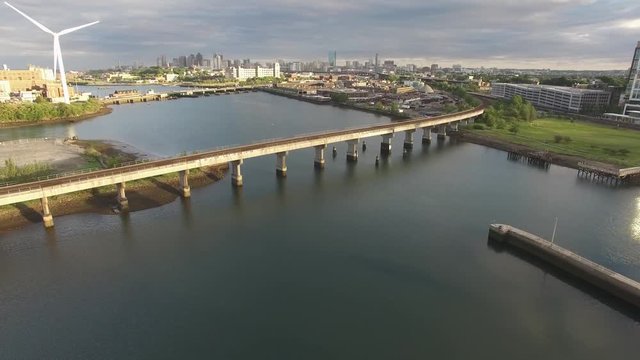 Aerial shot of railroad bridge over water with a spinning windmill and Boston skyline in the background