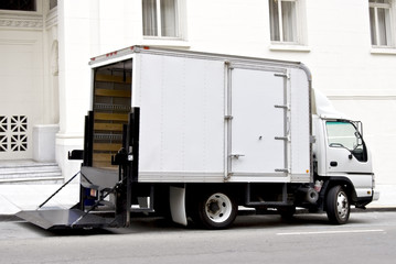 Rear and side view of white delivery van in front of white building.