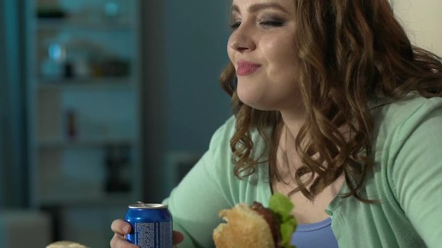 Young woman enjoying her burger and looking at it with admiration during movie