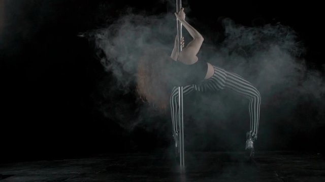 The girl is dancing Pole Dance on dark backgroun, in studio with smoke