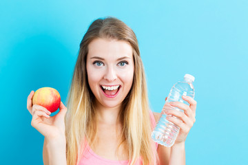 Happy young woman holding apple and water