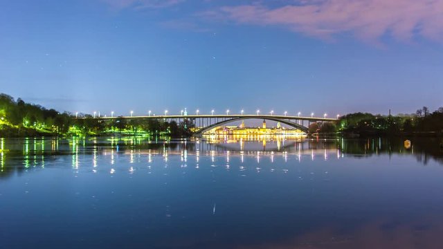 Tranquil bay and arch bridge at night 4K Time Lapse Tilt. Stockholm cityscape in background, beautiful reflections in the water