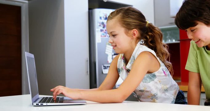 Siblings using laptop in kitchen