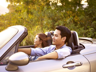 young asian couple riding in a convertible car