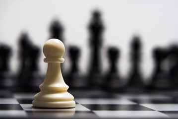 White pawn against the background of dark chess pieces - obrazy, fototapety, plakaty