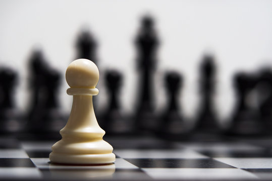 White pawn against the background of dark chess pieces