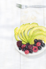 Healthy breakfast ingredients avocado slices with mix berries and honey.