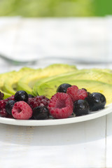 Healthy breakfast ingredients avocado slices with mix berries and honey.
