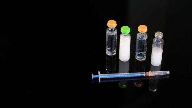 Four vial of insulin and disposable insulin syringe on black background, close-up. Set for diabetic.