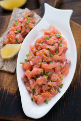 Closeup of salmon tartar served in a white plate, selective focus, vertical shot