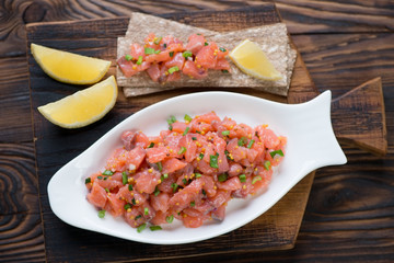 White plate with salmon tartar in a rustic wooden setting, above view