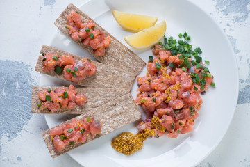 Above view of a white glass plate with salmon tartare on a white concrete background, horizontal shot
