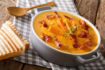 Healthy sweet potato cream soup with bacon and herbs in a saucepan and toast closeup. horizontal