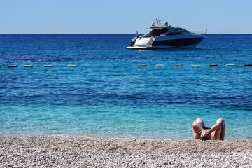 Fototapeta na wymiar The man covered his face with his hands, lies on a white beach, in a clear transparent sea stands a yacht