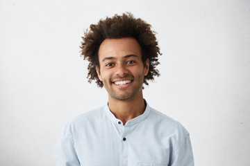 Cheerful African guy with narrow dark eyes and fluffy hair dressed in elegant white shirt having...