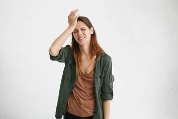 Naklejka premium Frustrated brunette woman wearing casual clothes holding hand on forehead being depressed regreting what she done having headache. Confused female with frowned face looking stressful having some pain