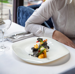 Woman in a restaurant eating a beautiful fish salad with fruits. Restaurant food concept.
