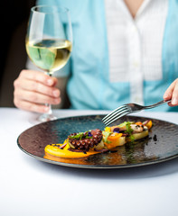 Woman is eating an octopus and drinking wine in a restaurant. Restaurant food concept.