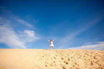 Little active girl  walking, running, jumping, having fun along the sand on the beach against the background blue sky in summer vacation