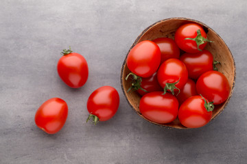 Small plum tomatoes in a wooden bowl on a gray background.