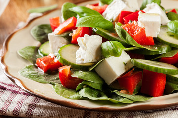 Fresh spinach salad with feta, cucumber and red paprika on a plate.