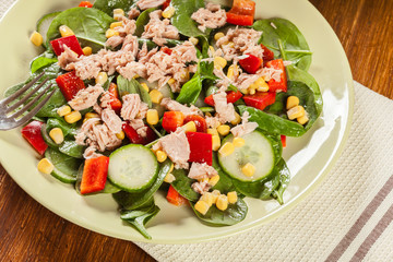 Fresh spinach salad with tuna, cucumber, corn, and red paprika on a plate