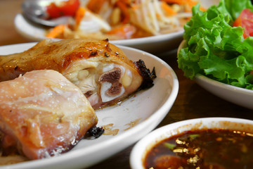 Thai food grilled chicken and salted egg papaya salad (somtum) with vegetable and sauce in white dish on wood table for lunch or dinner at thai restaurant