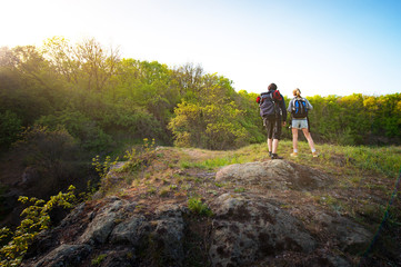 Fototapeta premium Couple of backpackers or hikers stands on mountain top at sunset or sunrise time and looking at sky. Travel concept.