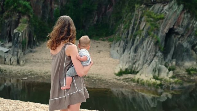 A young mother is walking by a small river with her baby