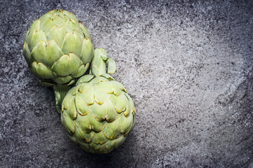 Fototapeta premium Green Artichokes on gray concrete background, top view. Superfood concept