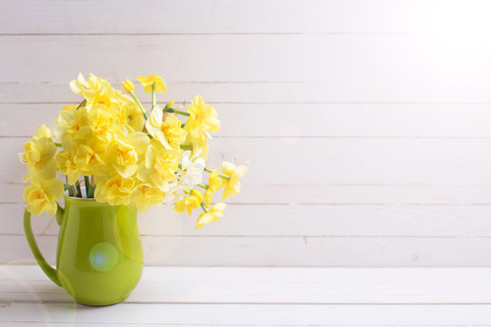 Bright yellow spring daffodils or narcissus flowers in pitcher  wooden background.